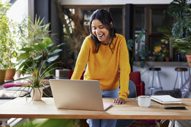 Glückliche Geschäftsfrau mit Laptop auf dem Schreibtisch im Loftbüro - BSZF02325