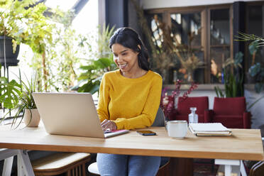 Smiling freelancer working on laptop sitting at desk in loft office - BSZF02329