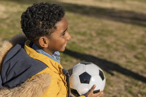 Glücklicher Junge im Parka-Mantel, der einen Fußball im Park hält - JCCMF09883