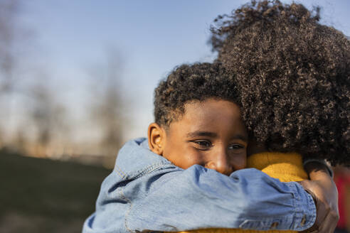 Junge umarmt Mutter im Park an einem sonnigen Tag - JCCMF09896