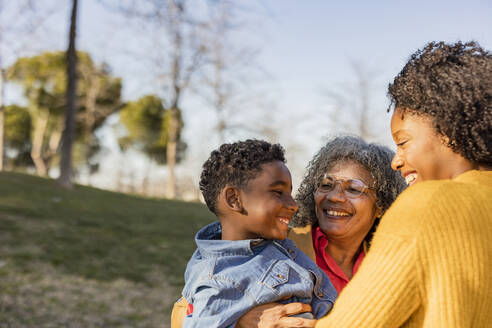 Glückliche ältere Frau mit Enkel, der sich mit seiner Mutter im Park amüsiert - JCCMF09900