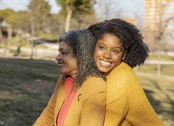 Happy young woman sitting with mother in park - JCCMF09902