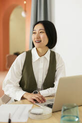 Happy businesswoman with short hair sitting at desk in office - EBSF02936