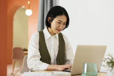 Lächelnde Geschäftsfrau mit kurzen Haaren bei der Arbeit am Laptop im Büro - EBSF02937