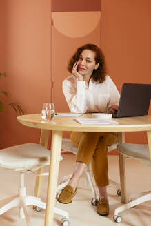 Geschäftsfrau mit Hand am Kinn sitzt am Schreibtisch im Büro - EBSF02968