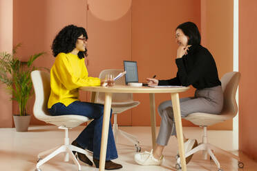 Lächelnde Geschäftsfrauen arbeiten zusammen am Schreibtisch im Büro - EBSF02974