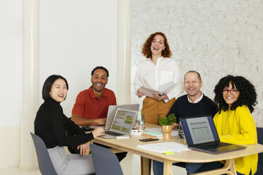 Glückliche Geschäftsleute sitzen mit Laptops am Schreibtisch im Büro - EBSF02981