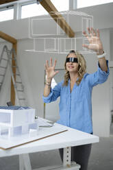 Smiling architect wearing virtual reality simulator examining house model over table - HMEF01582