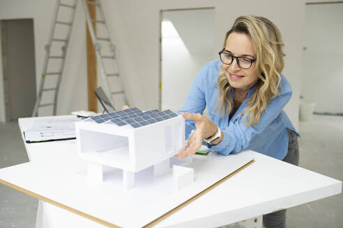 Smiling mature architect examining model home at desk - HMEF01585