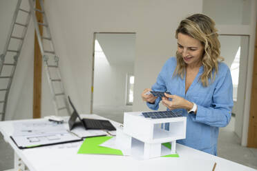 Lächelnder Architekt bei der Arbeit an einem Wohnmodell am Schreibtisch - HMEF01588