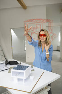 Architect wearing virtual reality simulator gesturing and examining house model at site - HMEF01594
