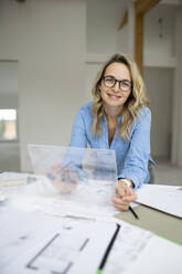 Smiling mature architect with transparent tablet PC at desk - HMEF01599