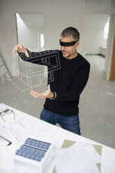 Älterer Architekt, der einen Virtual-Reality-Simulator trägt und ein Modellhaus auf der Baustelle untersucht - HMEF01606