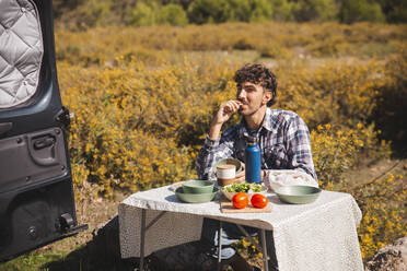 Mann isst Essen am Campingtisch an einem sonnigen Tag - PCLF00268
