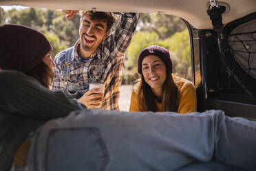 Happy friends taking to woman in trunk of campervan - PCLF00272