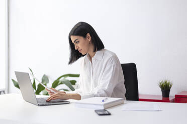 Geschäftsfrau mit Dokument tippt auf Laptop am Schreibtisch - LMCF00230