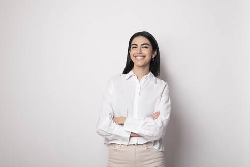 Smiling woman with arms crossed standing against white background - LMCF00235