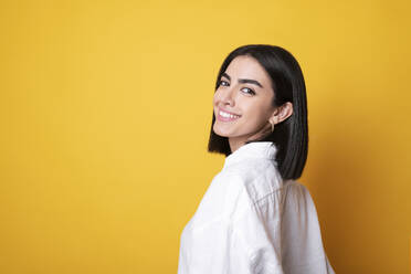 Smiling young woman standing against yellow background - LMCF00241