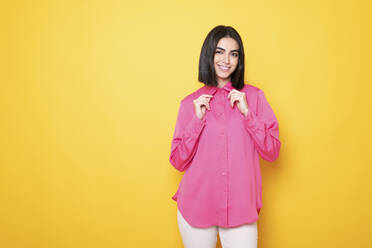 Glückliche junge Frau in rosa Hemd vor gelbem Hintergrund - LMCF00253