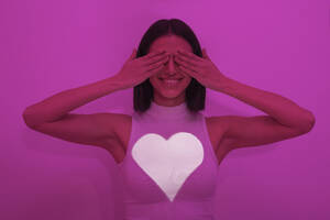 Glückliche Frau, die ihre Augen vor einem rosa Hintergrund bedeckt - LMCF00273