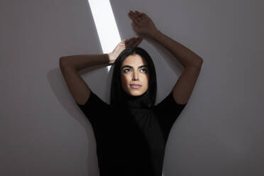 Nachdenkliche junge Frau mit Licht im Gesicht vor einer Wand - LMCF00279