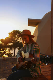 Lächelnde Frau spielt Gitarre bei Sonnenuntergang - SYEF00267