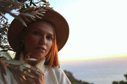 Frau mit Hut in der Nähe eines Olivenbaums bei Sonnenuntergang - SYEF00271