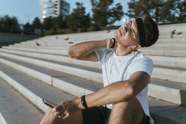 Young man stretching neck sitting on steps - ANNF00084