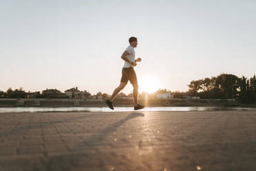 Junger Mann läuft bei Sonnenuntergang auf dem Fußweg - ANNF00095