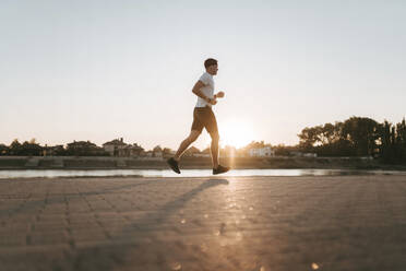 Young man running on footpath at sunset - ANNF00095