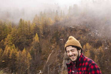 Happy young man standing on mountain in foggy weather - PCLF00282