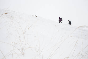 Playful father with children sledding on snowy hill against sky during  vacation stock photo