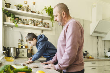 Grandfather with grandson preparing paper bags on kitchen counter - OSF01448