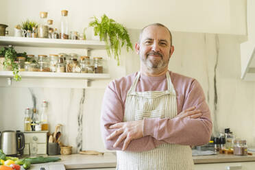 Smiling man with arms crossed standing in kitchen at home - OSF01450