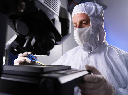Engineer examining computer chip through microscope in laboratory - CVF02342