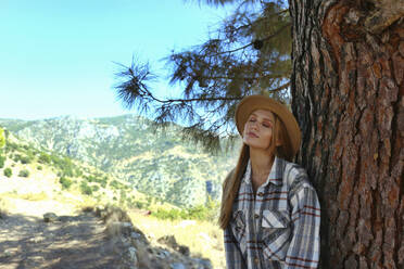 Junge Frau mit Hut, die sich auf einem Baumstamm ausruht - SYEF00276