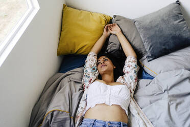 Thoughtful woman with arms raised lying on bed at home - JJF00450
