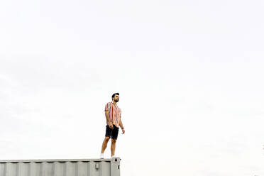 Man standing on top of container home under sky - JJF00501