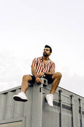 Contemplative man sitting on top of container home - JJF00502