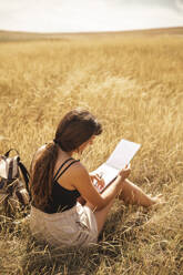 Junge Frau mit Skizzenblock auf trockenem Gras sitzend - PCLF00287