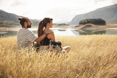 Man sitting with arm around girlfriend on dry grass - PCLF00293