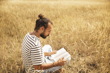 Man reading book sitting in field - PCLF00297