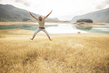 Carefree man jumping in front of lake - PCLF00302
