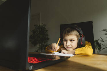 Boy wearing headset studying online through laptop at home - OSF01453