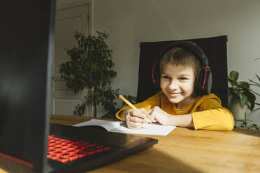 Lächelnder Junge mit Headset, der zu Hause mit seinem Laptop online lernt - OSF01454