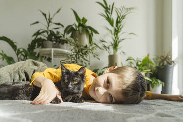 Smiling boy lying on carpet with black cat - OSF01457