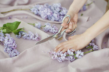 Hands of woman cutting linen fabric with scissors - ONAF00441