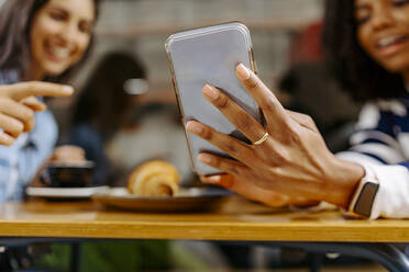 Young woman showing smart phone to friend at cafe - JJF00510