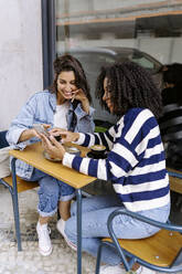 Freunde unterhalten sich in einem Straßencafé über ihr Smartphone - JJF00515