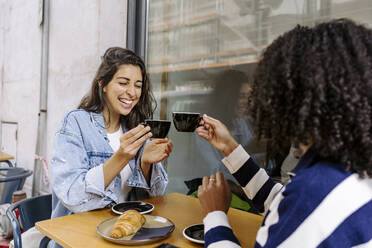 Cheerful young friends toasting coffee cup and enjoying at sidewalk cafe - JJF00517